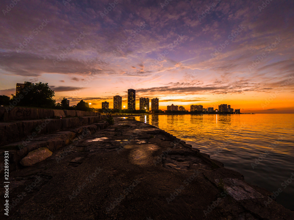 Gorgeous sunset photograph looking across Lake Michigan at Foster Beach to the highrise buildings and colorful blue purple and orange colored sky on the horizon.