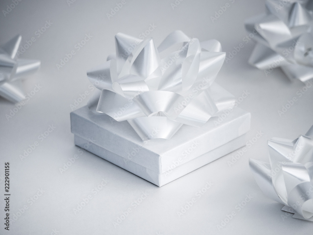 Close-up photograph of a small white glossy gift box with a manufactured shiny white ribbon bow on top isolated on a white background. Close-up photograph of a small white glossy gift box with a manufactured shiny white ribbon bow on top isolated on a white background.