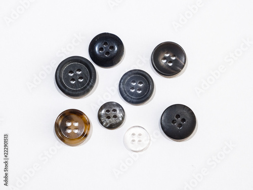 Close up view of several four hole sewing or clothing buttons of random shape color and size isolated on a white background.