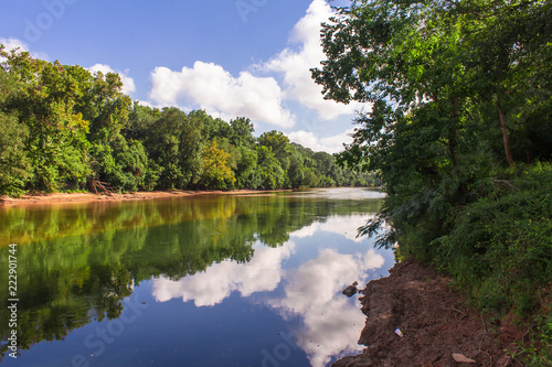 Reflections of clouds on river lined with green trees photo