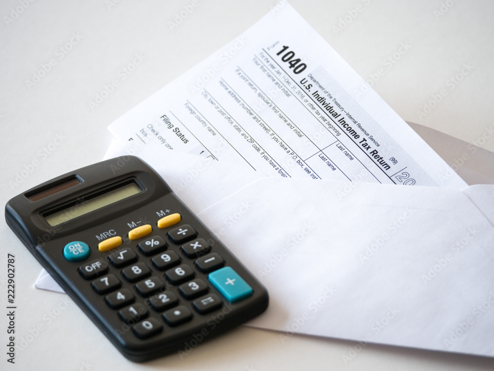 Closeup image of a stuffed envelope with the federal 1040 individual income tax return with black calculator isolated on a white background for tax season background or wallpaper. Closeup image of a stuffed envelope with the federal 1040 individual income tax return with black calculator isolated on a white background for tax season background or wallpaper.
