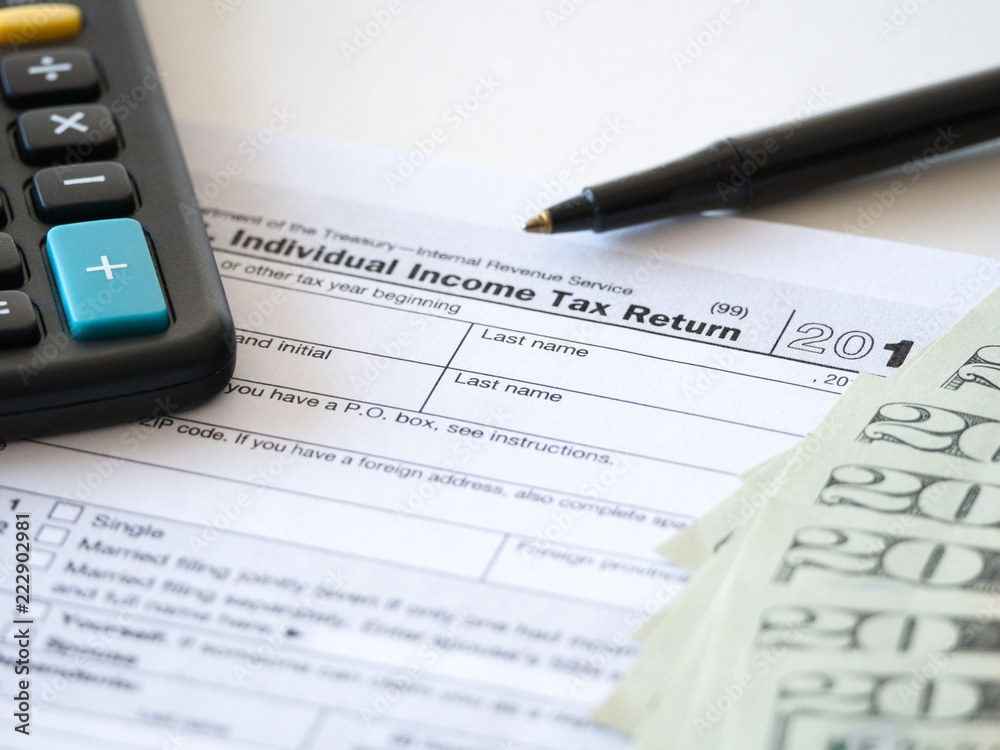 Fototapeta premium Close-up photograph of a hard copy of an individual income tax return with black calculator and 20 dollar bills piled up representative of United States federal tax cuts and savings this year.
