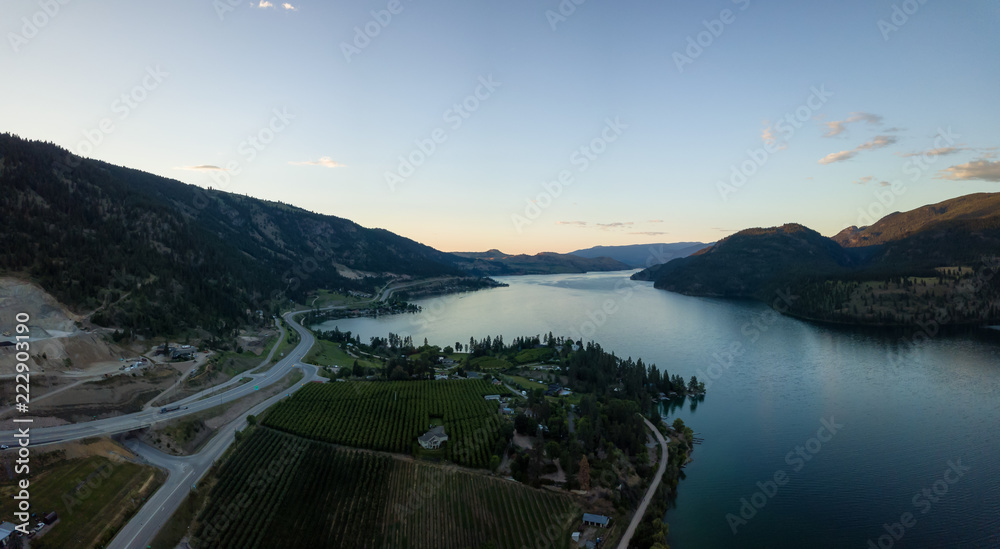 Aerial panoramic view of homes near a lake during a vibrant summer sunset. Located near Kelowna and Vernon, BC, Canada.