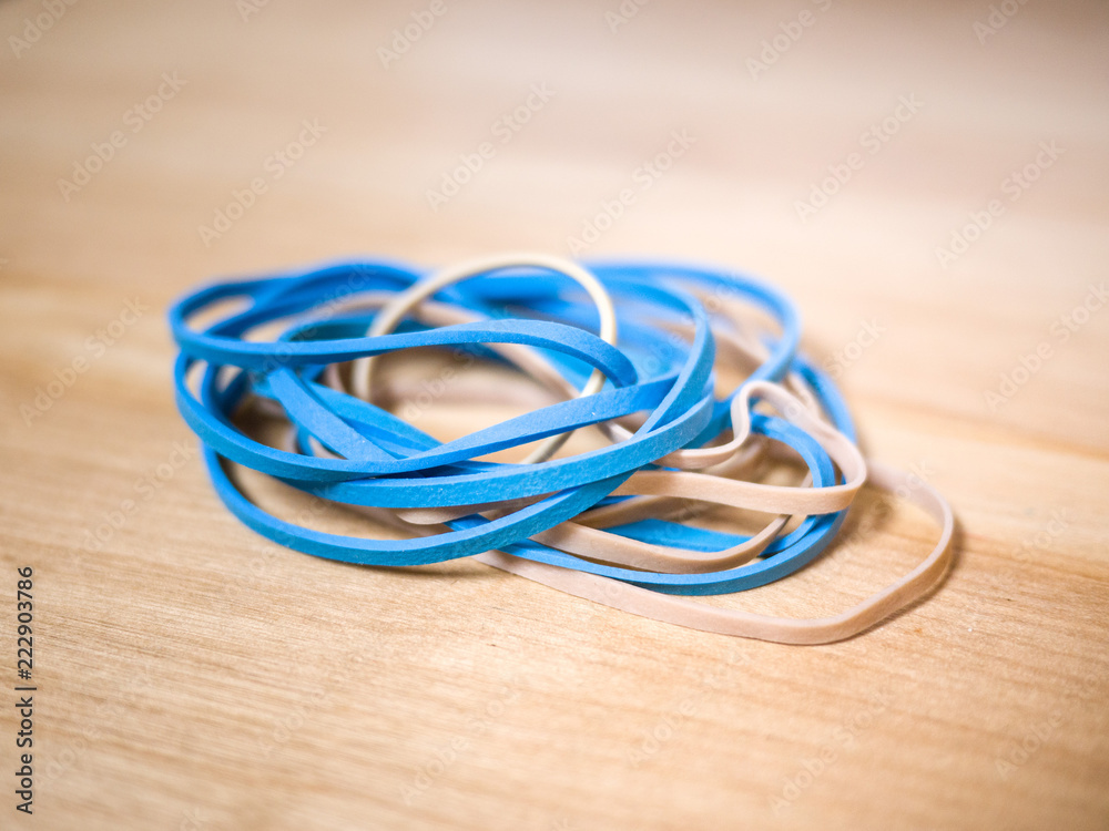 Close up macro photograph of blue and cream colored rubber band office supplies stacked on on a light colored wood grain desk background. Close up macro photograph of blue and cream colored rubber band office supplies stacked on on a light colored wood grain desk background.