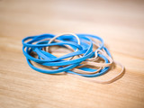 Close up macro photograph of blue and cream colored rubber band office supplies stacked on on a light colored wood grain desk background.
