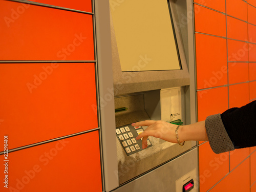 Woman hand near keyboard of postomat terminal near storage cells for order delivery photo