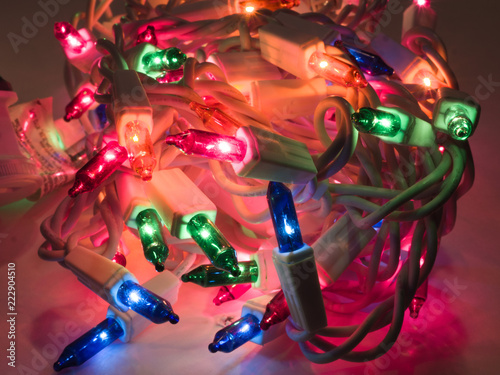 Close up photograph of a pile of colored Christmas lights including green, blue, red, and orange making a festive holiday background.