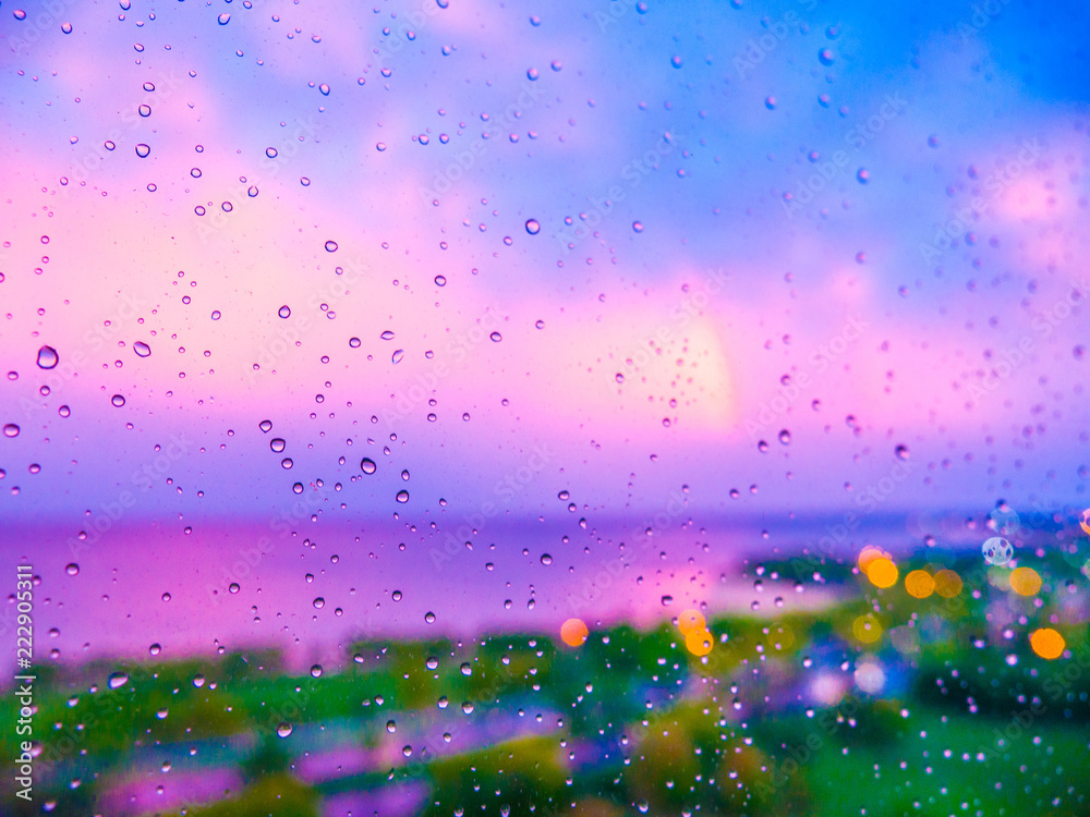 Colorful water droplets on the glass of a window during a rain storm at sunset
