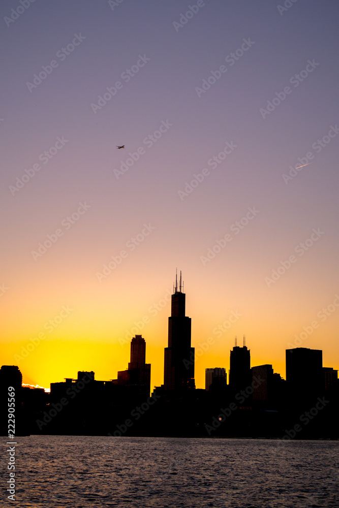 Chicago skyline picture during beautiful orange yellow sun as it lowers below the building silhouettes and the water of lake Michigan in the foreground