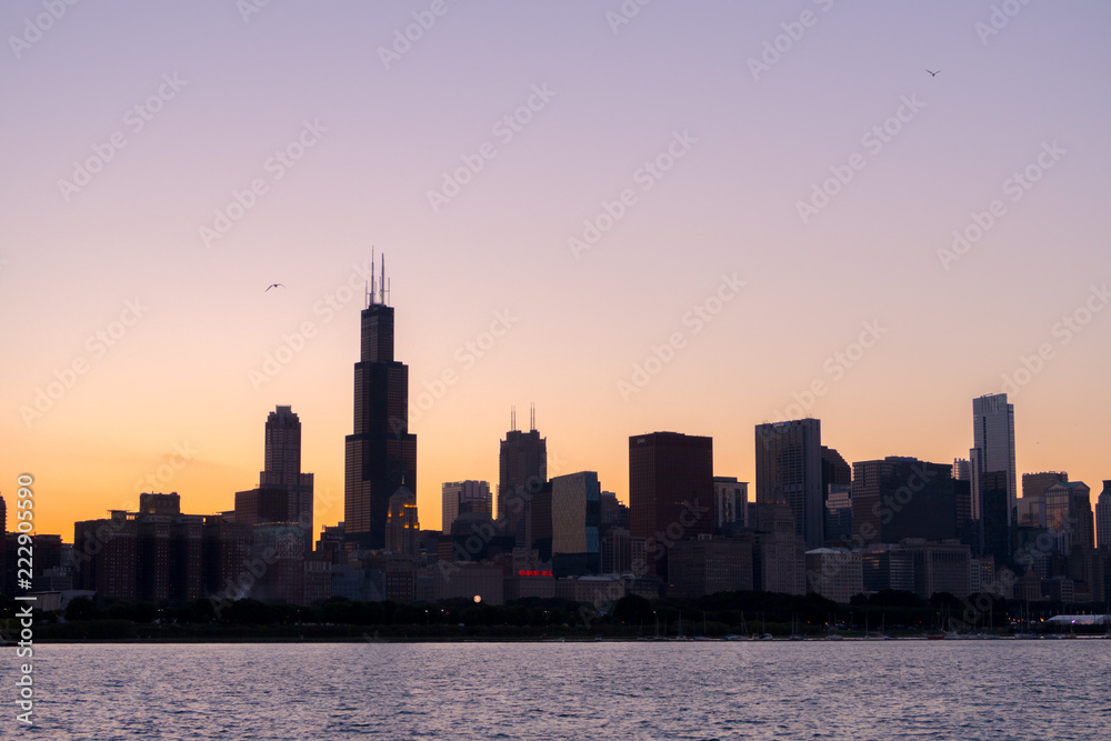 Chicago skyline picture during beautiful orange yellow sun as it lowers below the building silhouettes and the water of lake Michigan in the foreground