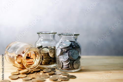 Coins in currency glass jars and spilling on wooden table. Saving money for future retirement. Financial business investment concept