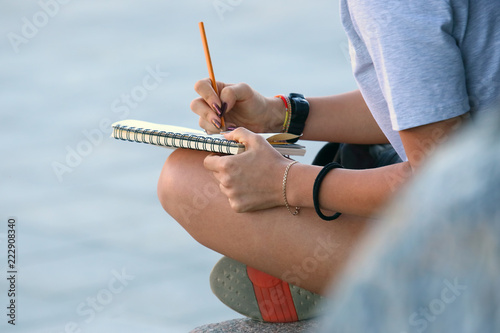 girl draws in a notebook sitting on the pavement