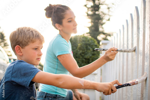 mother and son painting a white picket fence in the summer