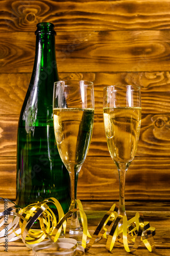 Bottle of champagne and two wineglasses decorated with golden ribbon on wooden table