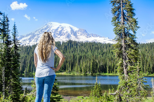 A woman hiking near a beautiful scenic mountain lake at Mount Rainier National Park in Washington USA. Looking up at the snow capped glacier during a day hike