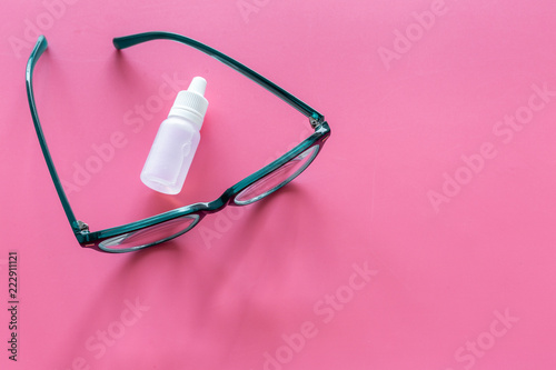 Eye health. Glasses with transparent optical lenses and eye drops on pink background top view copy space closeup