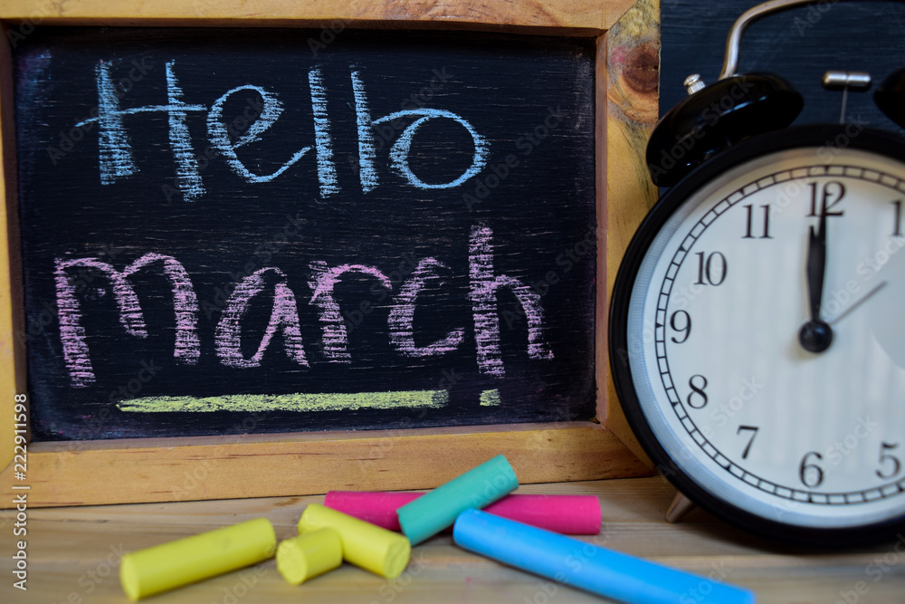 Hello march. Back to school concept. Alarm clock on wooden with blackboard on background Hello march. Back to school concept. Alarm clock on wooden with blackboard on background