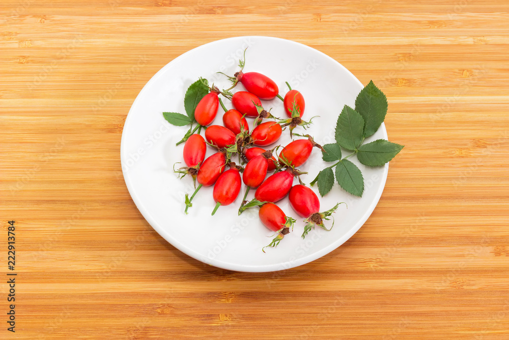 Red rose hips on white saucer on a wooden surface Red rose hips on white saucer on a wooden surface