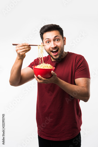 Indian/asian man eating hot noodles or ramen in a Red bowl with chopsticks