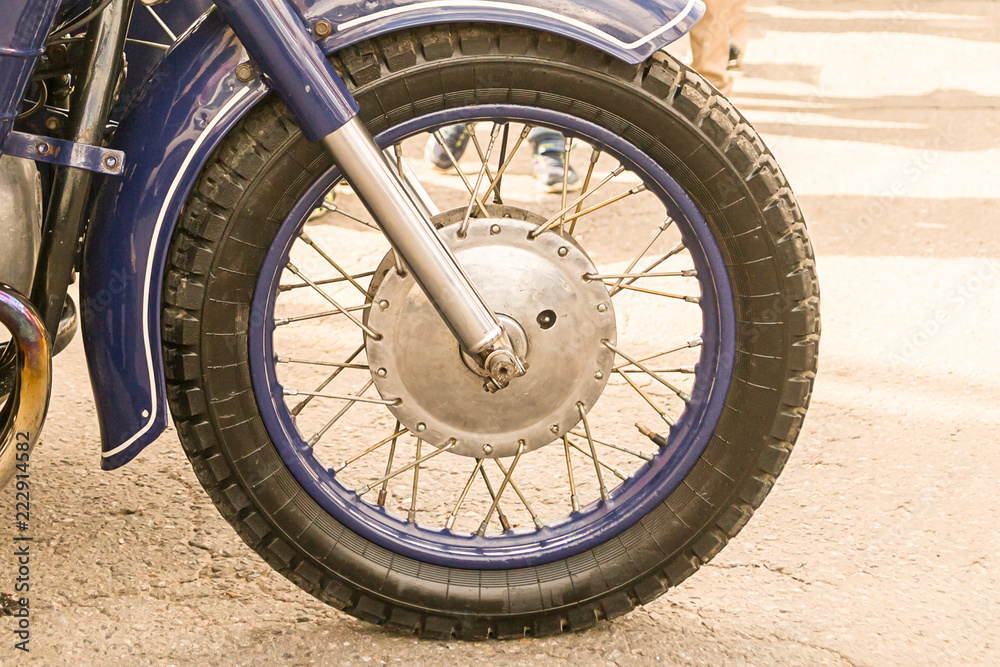 motorcycle front wheel with shiny chrome knitting needles with blue rim close-up on the asphalt background