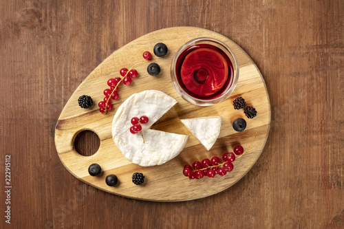 An overhead photo of Camembert cheese with a glass of red wine and fruits, on a dark rustic background with a place for text