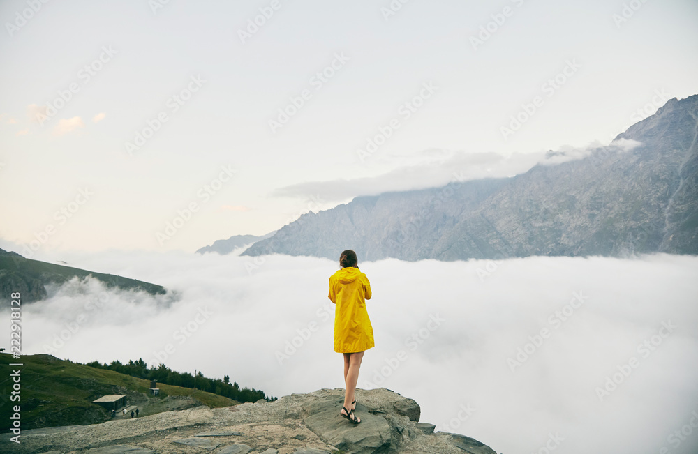 Obraz premium A young Girl in a yellow raincoat photographs the mountains. Georgia. Summer. August. Girl making a photo shoot of mountain. 
