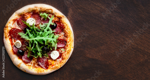 Hot pizza with Pepperoni Sausage on a dark background, top view. Italian Pizza on a rustic wooden table