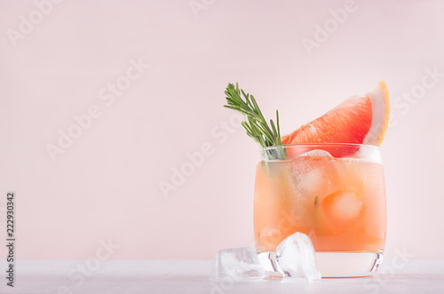 Cold grapefruit alcohol cocktail in misted glass with rosemary and grapefruits slice on pastel fashion pink background.