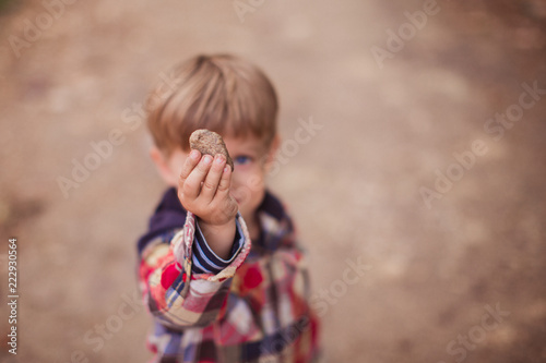 Close-up of the little boy who is holding the stone in hand outdoors