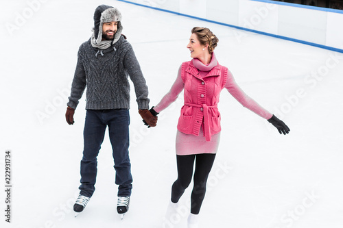 Happy couple holding their hand during ice skating in winter