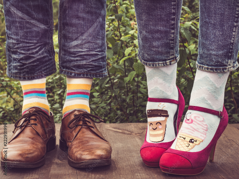 Men's and women's feet in stylish shoes, bright, colorful socks with stripes patterns and  pictures of ice cream on the wooden terrace on the background of green trees. Lifestyle, fashion, beauty, fun
