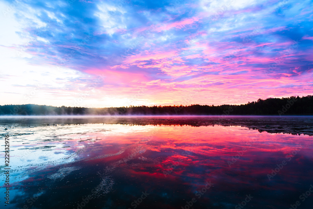 Bright colorful foggy sunset on the lake with clouds and reflections in Finland. Nature amazing sunrise background.
