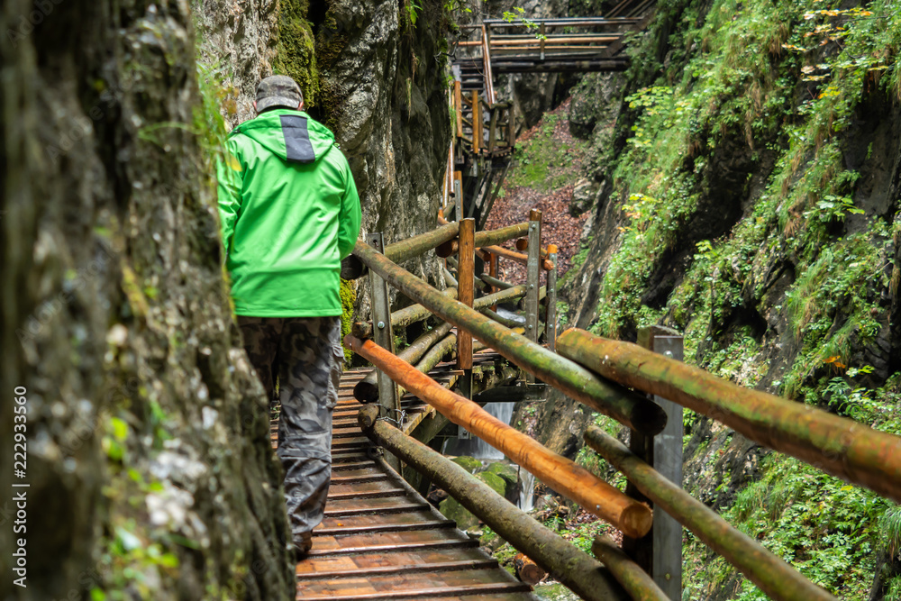 Man walks over wooden stairs through a water gorge in Austria