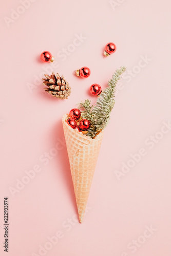 Creative minimalist composition with waffle cone with spruce and Christmas small red balls on a pink background.