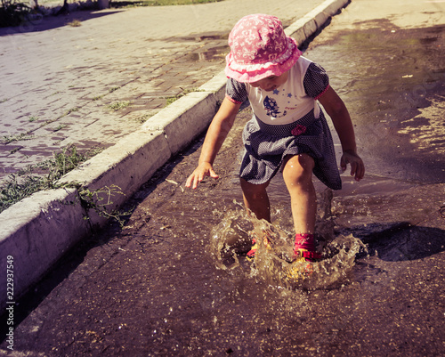 Fototapeta Naklejka Na Ścianę i Meble -  Cute baby sports and runs through the puddles on a summer sunny day
