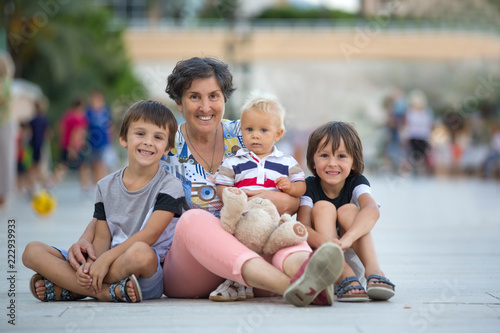 Grandmother with three grandchildren, sitting on the ground on the square in the city