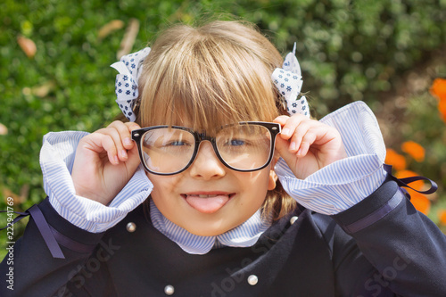 Portrait of a small cheerful blue-eyed girl first-class with screwed hair with bantikami and glasses in school uniform with a briefcase on September 1 photo