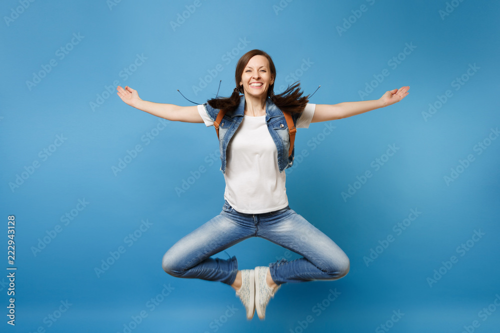 Full length portrait of young smiling woman student in denim clothes jumping spreading hands putting feets together isolated on blue background. Education in university. Copy space for advertisement. Full length portrait of young smiling woman student in denim clothes jumping spreading hands putting feets together isolated on blue background. Education in university. Copy space for advertisement.