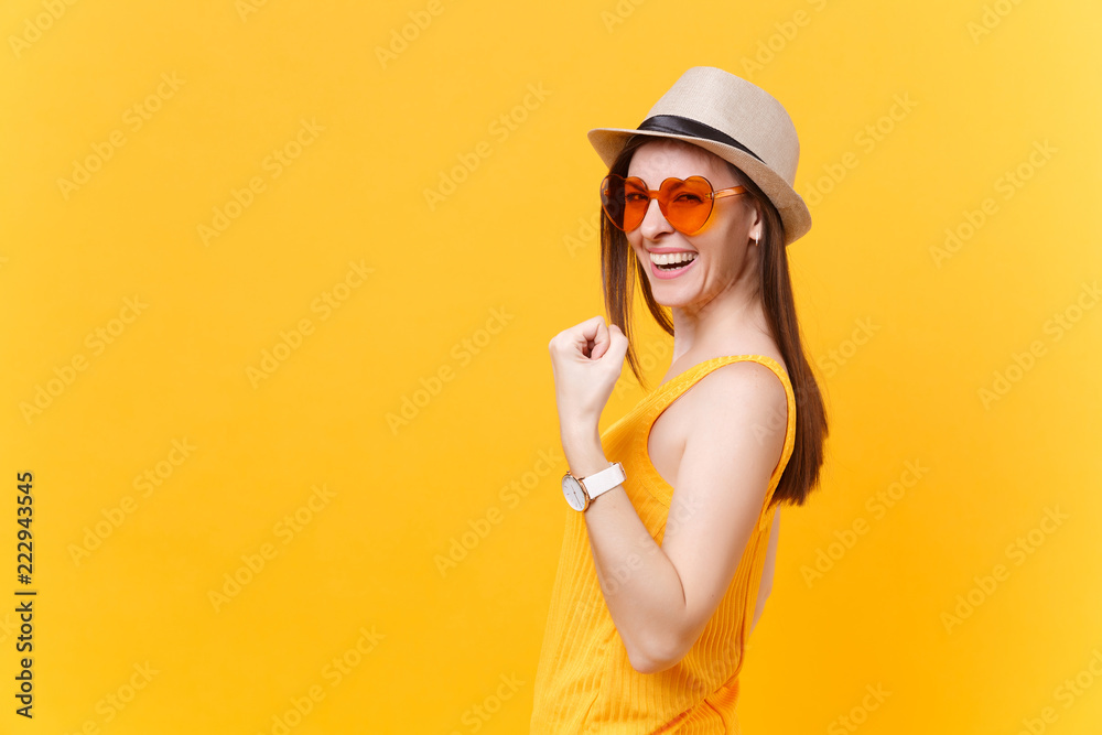 Portrait of smiling excited young woman in straw summer hat, orange glasses doing winner gesture, saying Yes isolated on yellow background. People sincere emotions lifestyle concept. Advertising area.