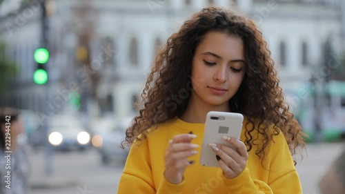 Teen girl in yellow pullower using smartphone texting messages a mobile phone, communicate in city photo