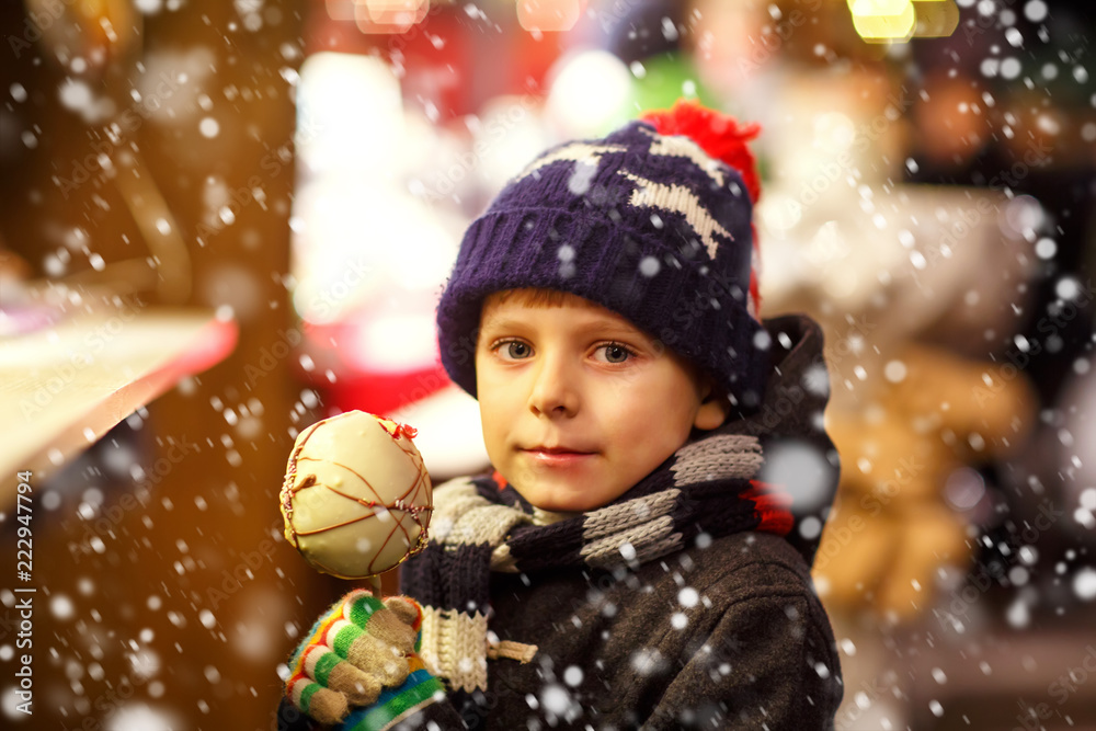 Happy child eating on apple covered with white chocolate on Christmas market