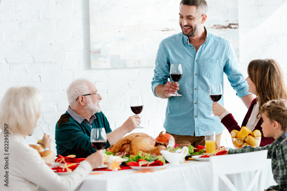 adult man with wine glass making toast while his family having holiday dinner on thanksgiving adult man with wine glass making toast while his family having holiday dinner on thanksgiving