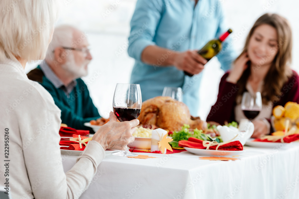 partial view of senior woman with wine glass celebrating thanksgiving with family at served table with turkey