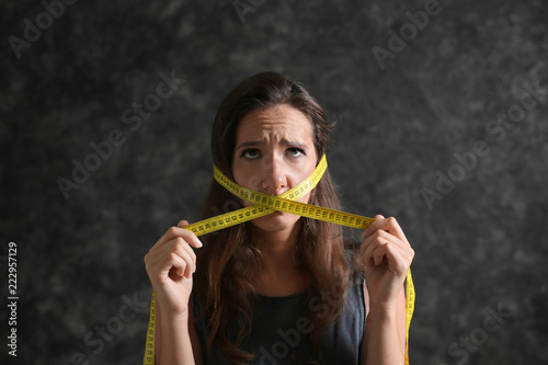 Woman with measuring tape around her mouth on dark background. Diet concept