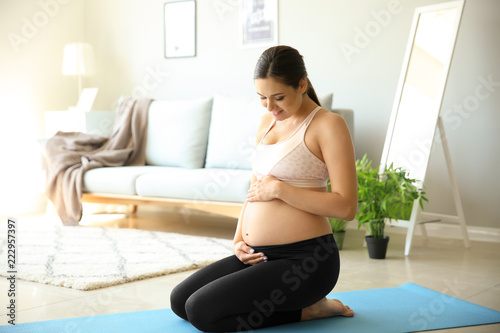 Young pregnant woman sitting on yoga mat at home
