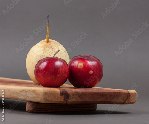 Wooden cutting board on grey background with fruits