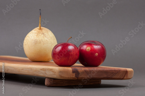 Wooden cutting board on grey background with pear and apples