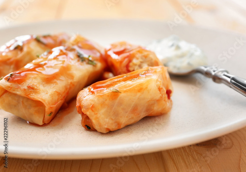 Plate with stuffed cabbage leaves in tomato sauce on wooden table, closeup