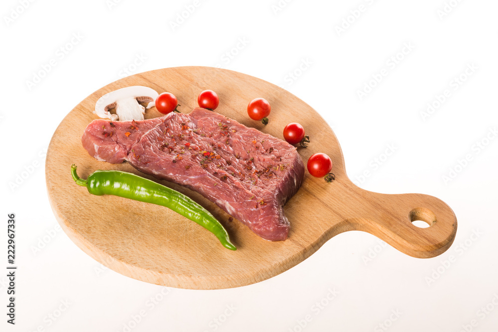 Uncooked steak with spices and vegetables on wooden plate