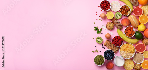 Organic food frame. Banner. Healthy breakfast ingredients. Oat and corn flakes, eggs, nuts, fruits, berries, toast, milk, yogurt, orange, banana, peach on pink background. Top view, copy space